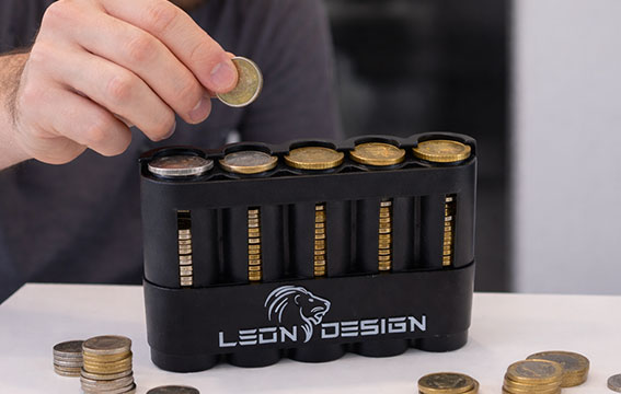 A hand places a coin into a black Leon Design coin holder.